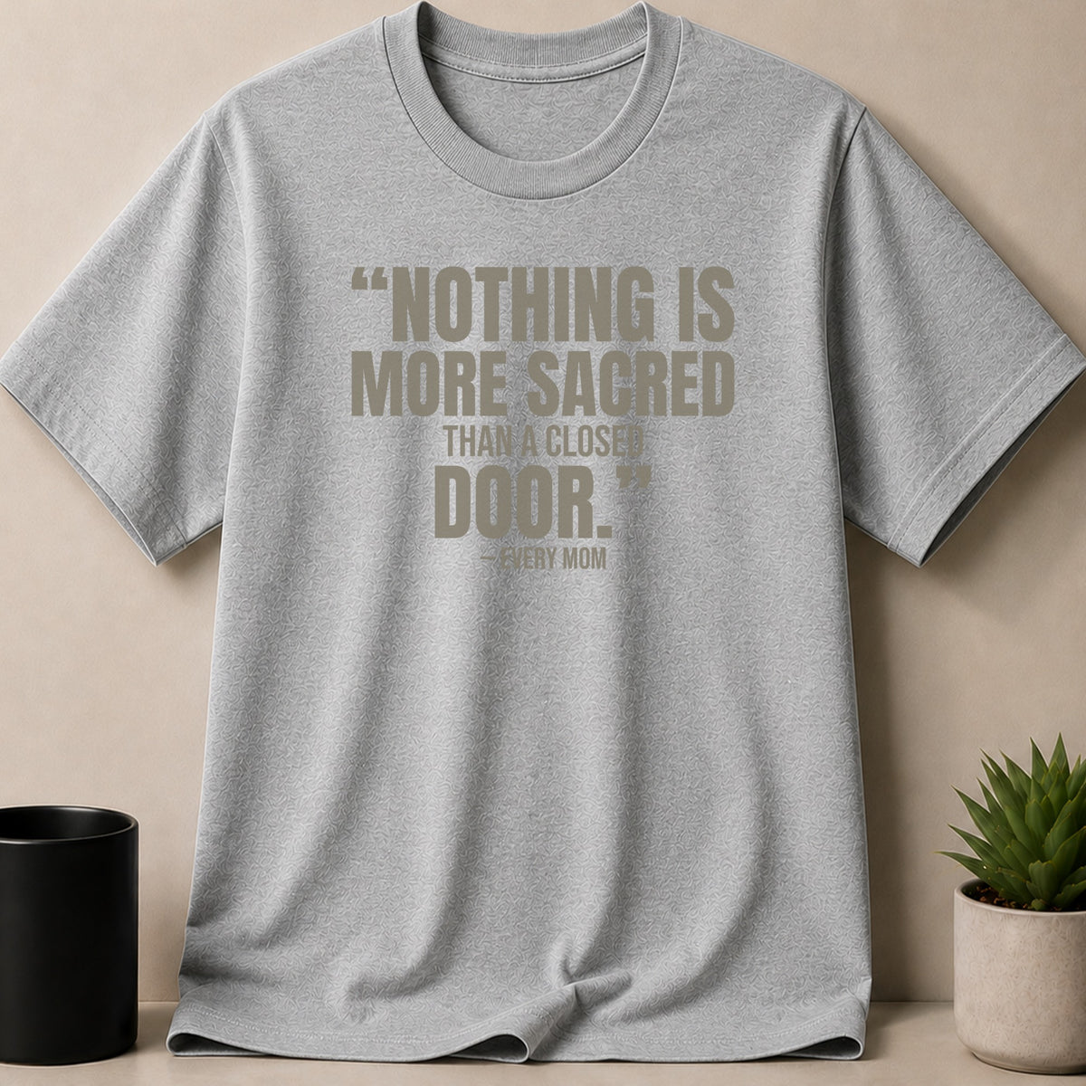 A grey t-shirt featuring the printed quote, "Nothing is more sacred than a closed door." – Every Mom.