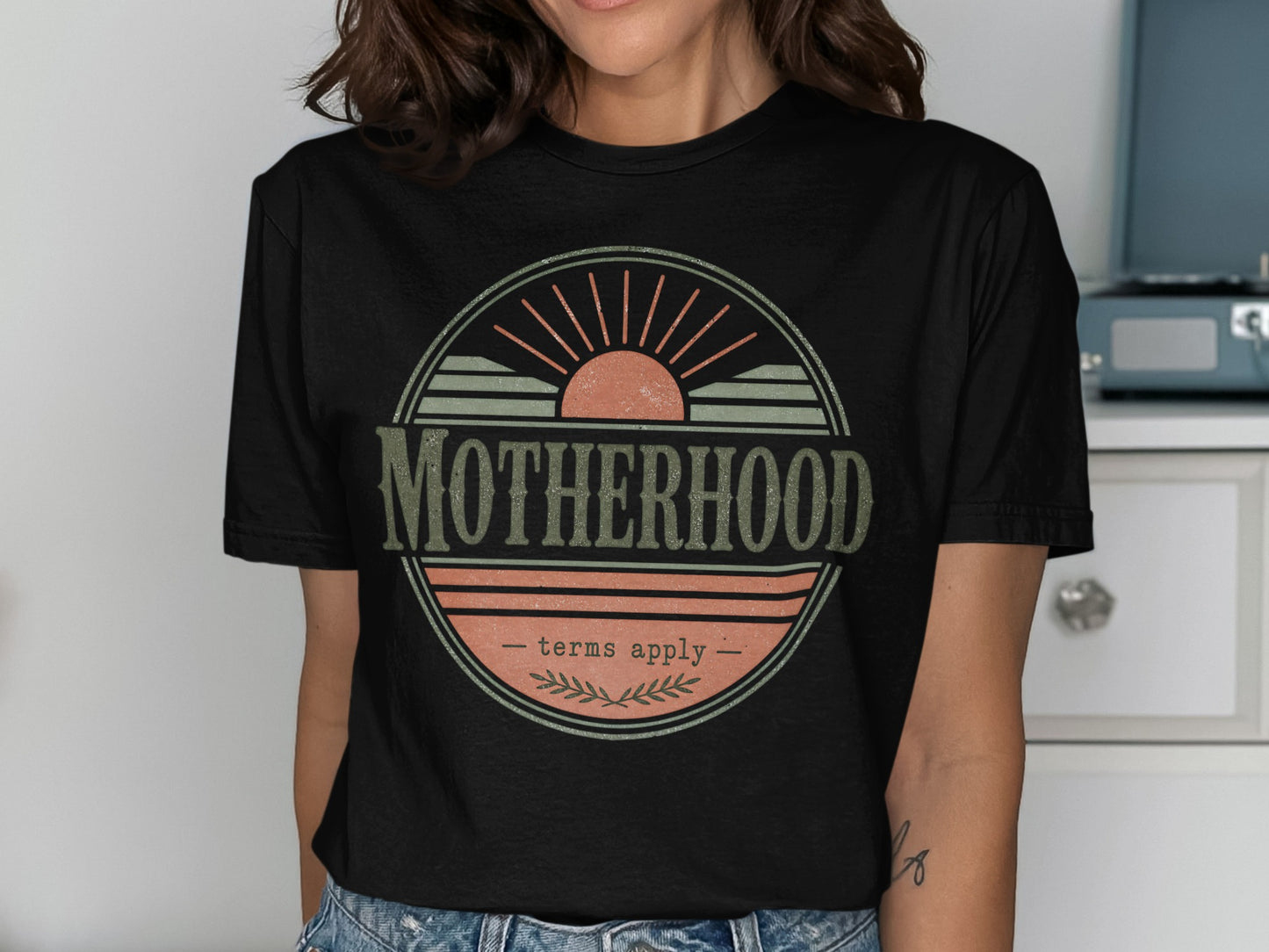 Black t-shirt with "MOTHERHOOD terms apply" graphic featuring a sunset and branches.