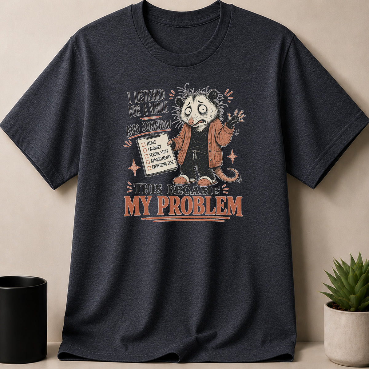Dark Heather t-shirt — T-shirt with opossum holding a checklist, text reads "This Became My Problem".