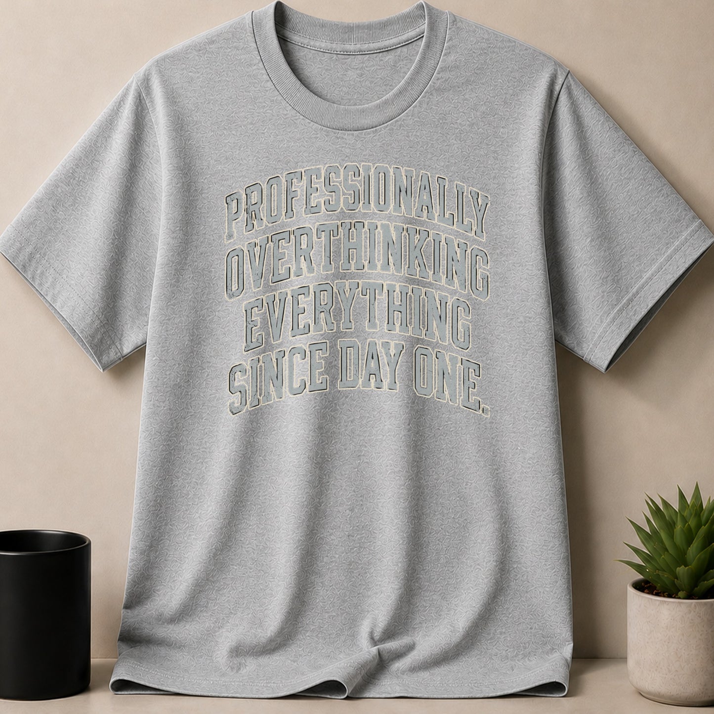 Grey t-shirt with "PROFESSIONALLY OVERTHINKING EVERYTHING SINCE DAY ONE." text.