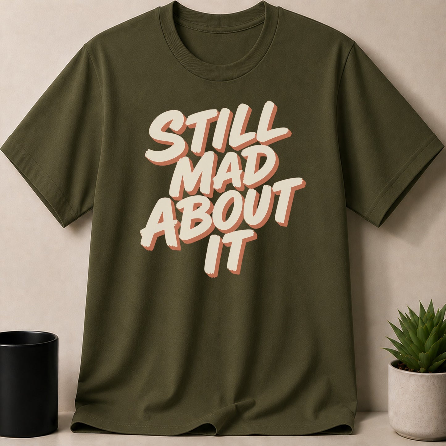 Olive green t-shirt with text "STILL MAD ABOUT IT".