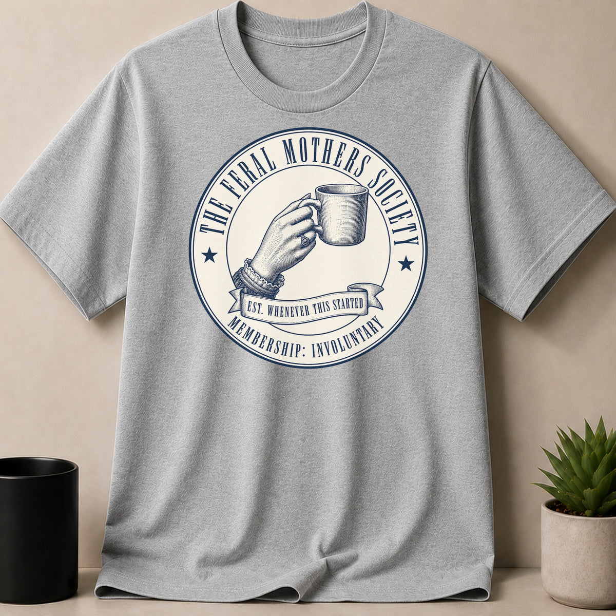 Light grey t-shirt with "The Feral Mothers Society" logo featuring a hand holding a mug.