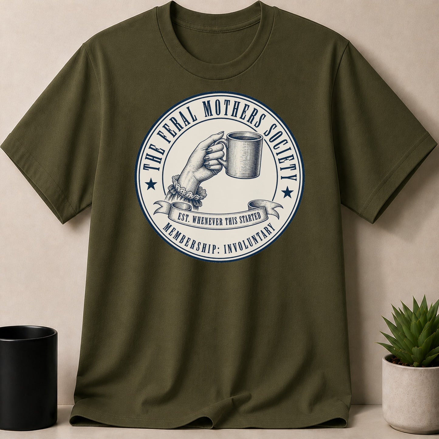 Olive green t-shirt with "The Feral Mothers Society" circular logo and "Membership: Involuntary" text.