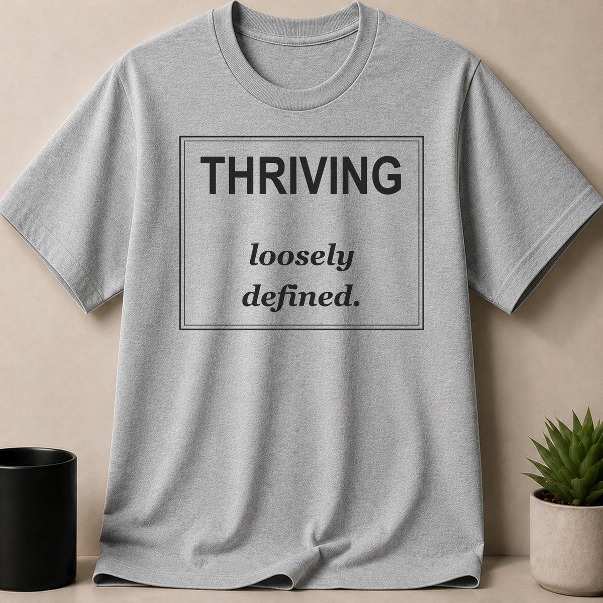Grey t-shirt with "THRIVING loosely defined." text in a black rectangle.