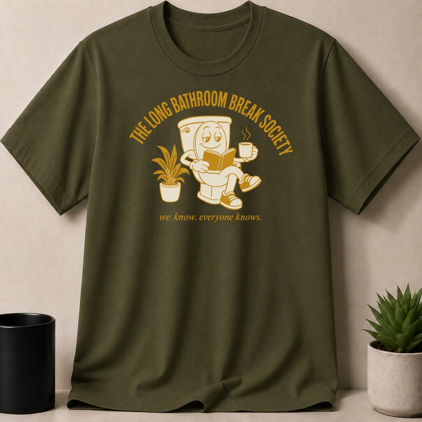 Olive t-shirt with cartoon toilet reading a book and holding coffee, text: "THE LONG BATHROOM BREAK SOCIETY we know. everyone knows."