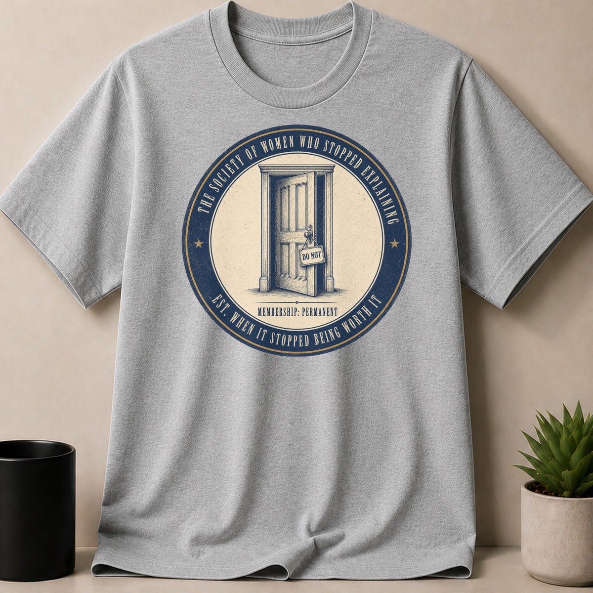 Grey t-shirt with circular graphic: "The Society of Women Who Stopped Explaining"