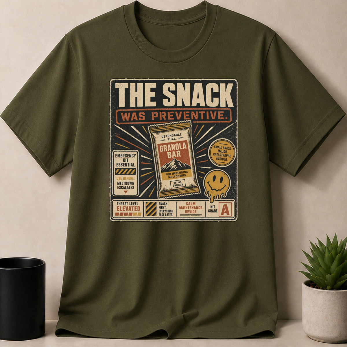 Military Green t-shirt — T-shirt graphic "The Snack Was Preventive" with a granola bar and smiley face.