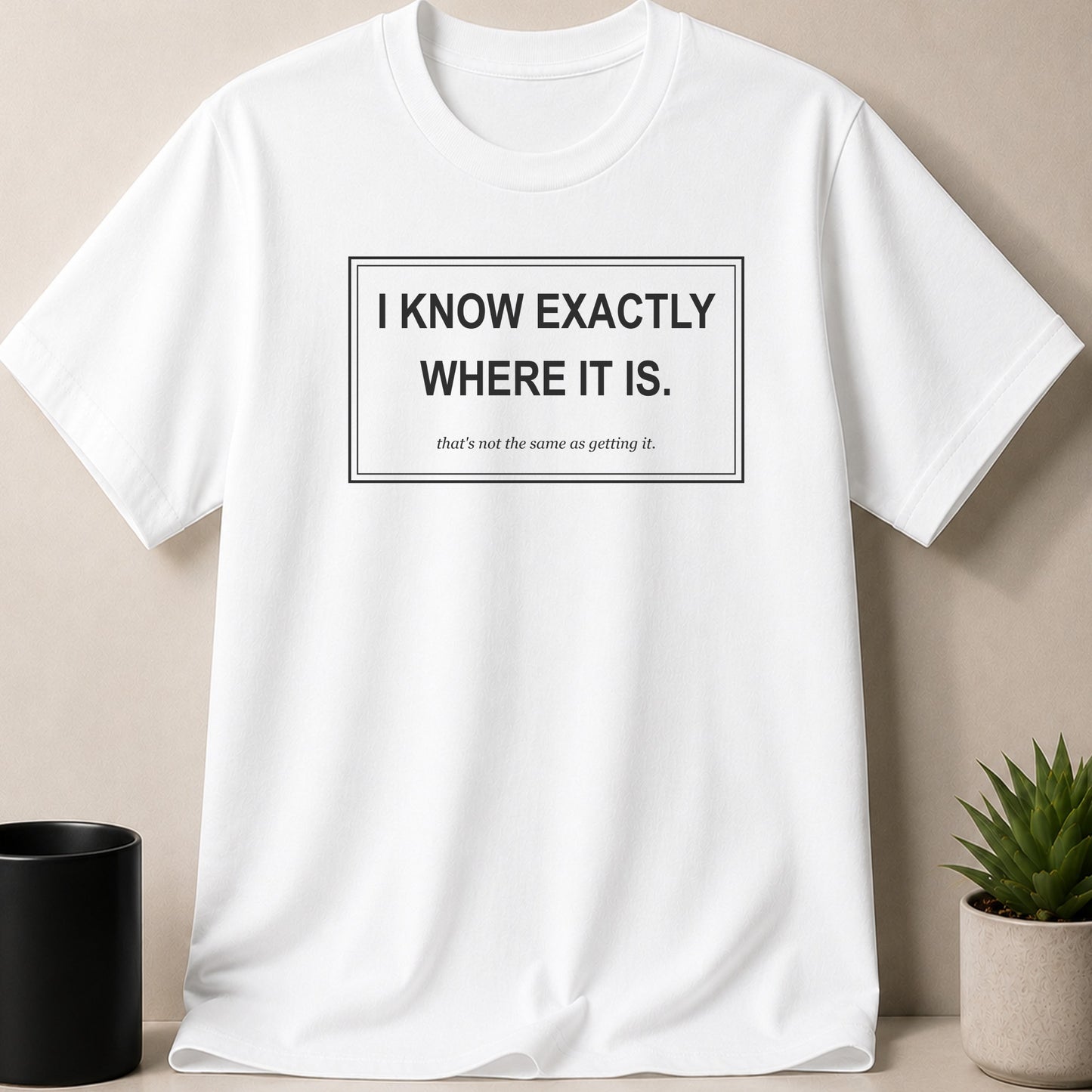 White t-shirt with black text "I KNOW EXACTLY WHERE IT IS. that's not the same as getting it."