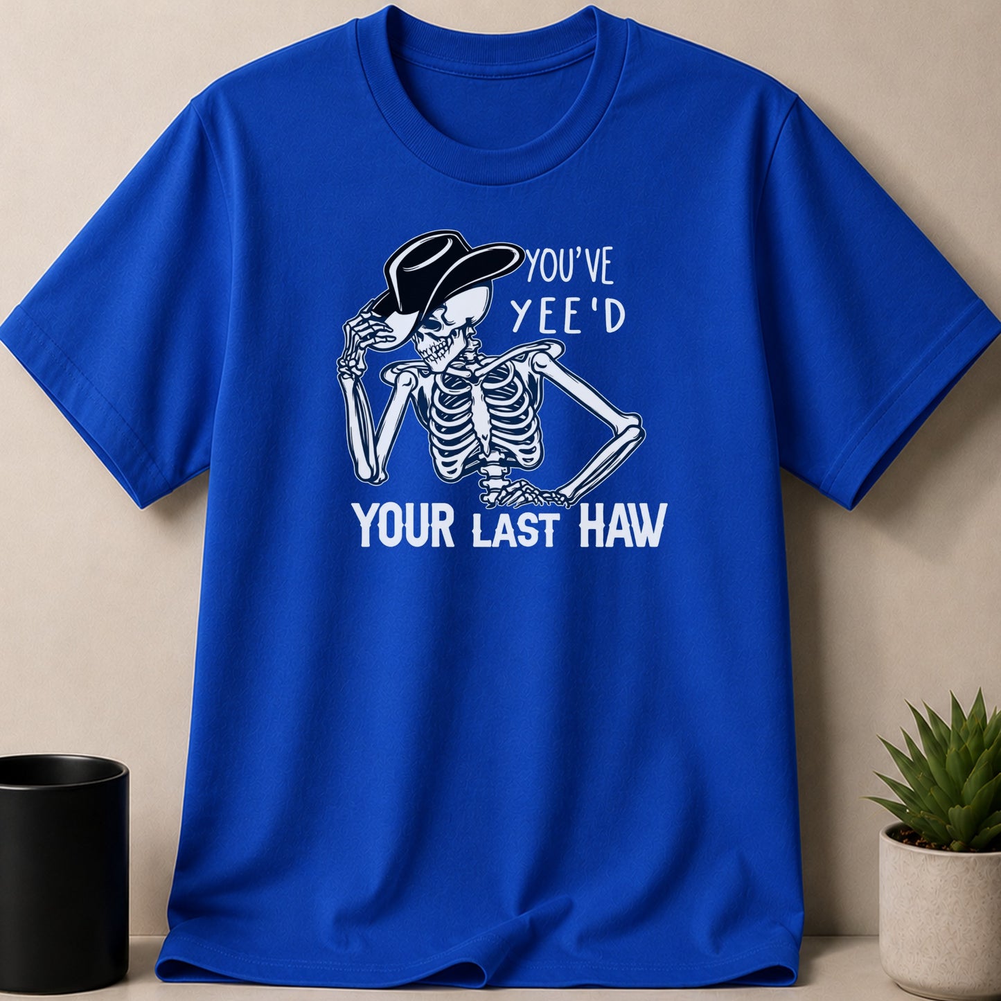 Skeleton wearing a cowboy hat on a blue t-shirt with text.