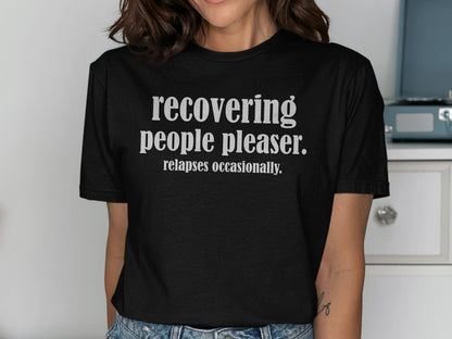 Black t-shirt with white text reading "recovering people pleaser. relapses occasionally."