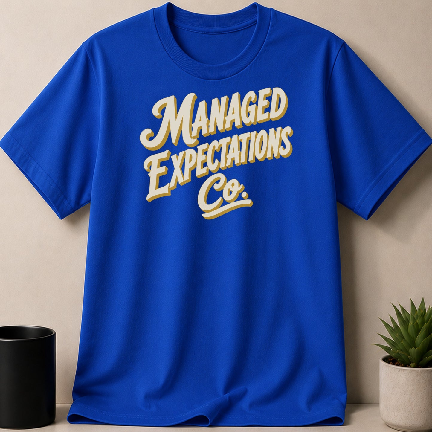 Blue t-shirt with "MANAGED EXPECTATIONS Co." text in cream and yellow.
