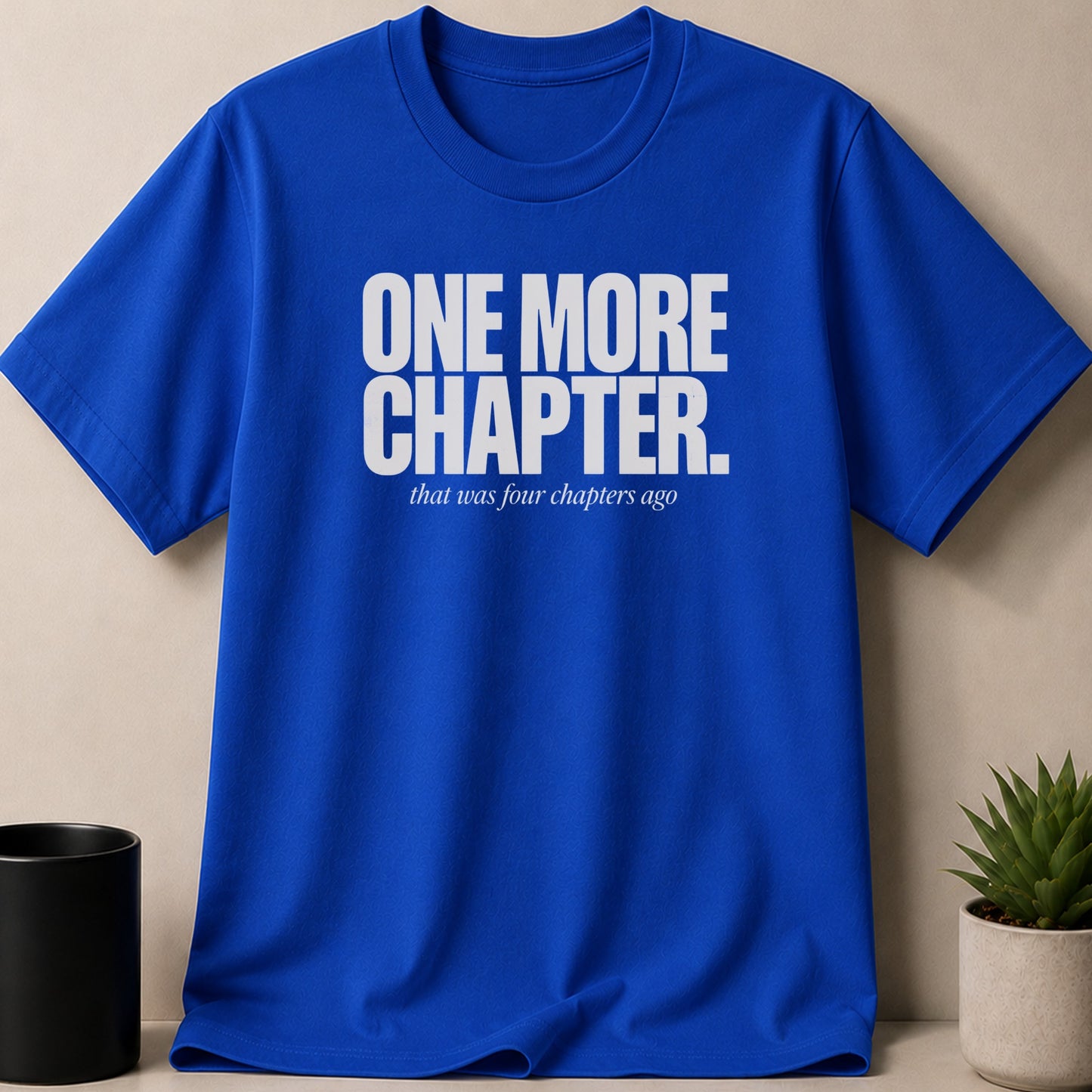 Blue t-shirt with white text "ONE MORE CHAPTER. that was four chapters ago."