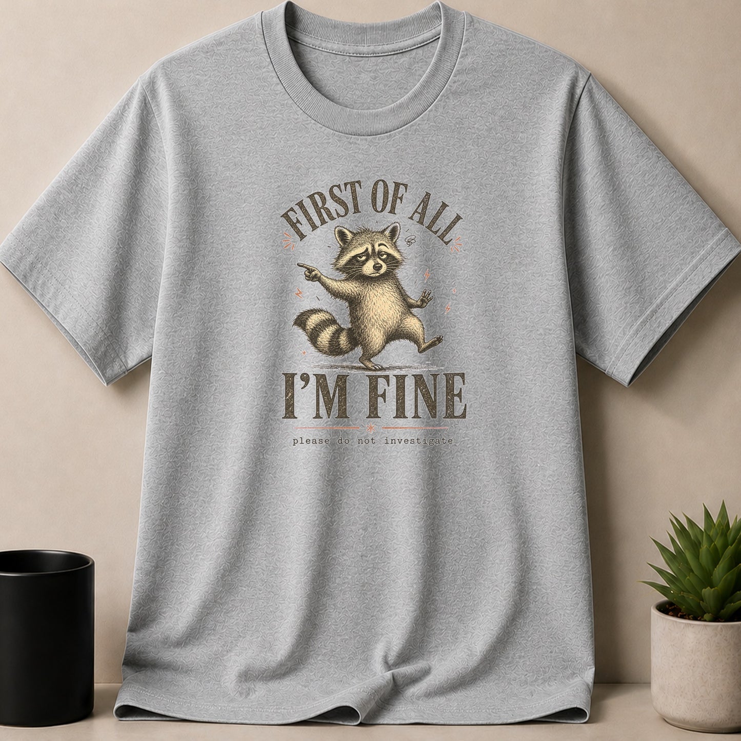 Light gray t-shirt with distressed graphic of a raccoon saying "First Of All, I'm Fine. Please Do Not Investigate."