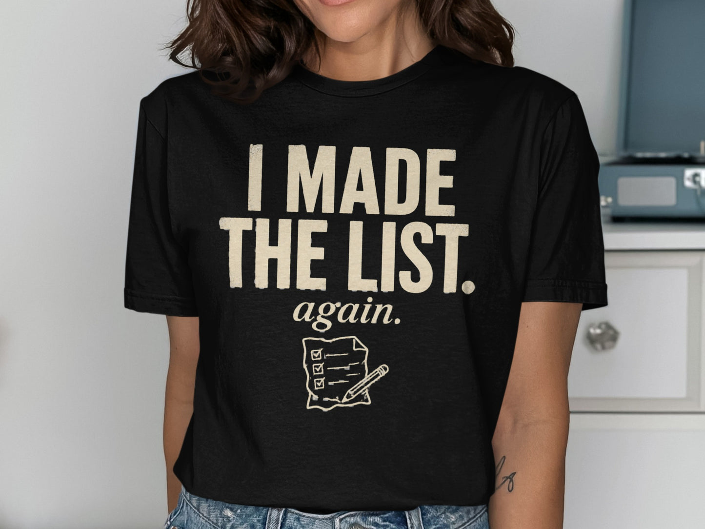 Black t-shirt with cream text "I MADE THE LIST. again." and a checklist graphic.
