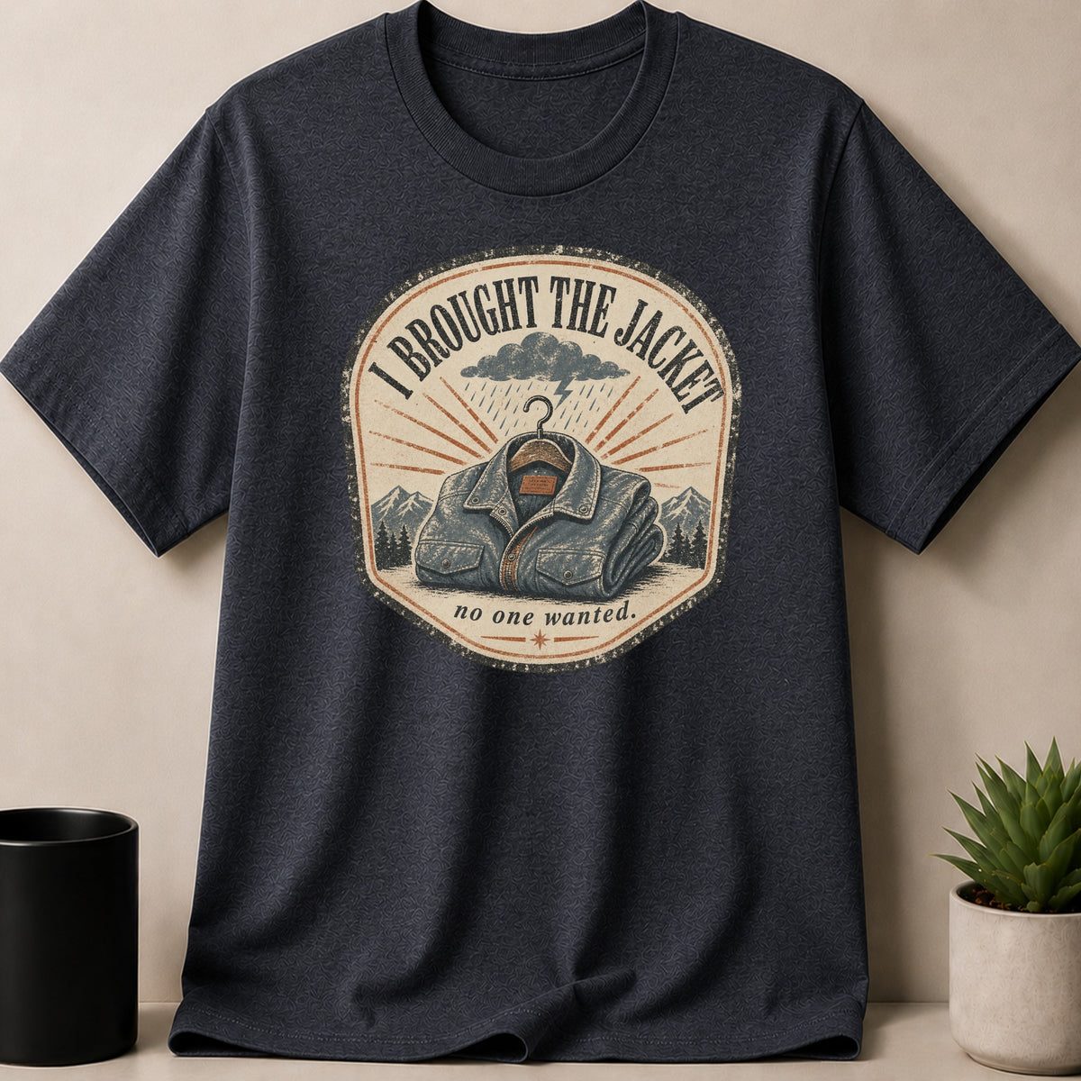 Dark grey t-shirt with circular graphic of a denim jacket, mountains, and text.