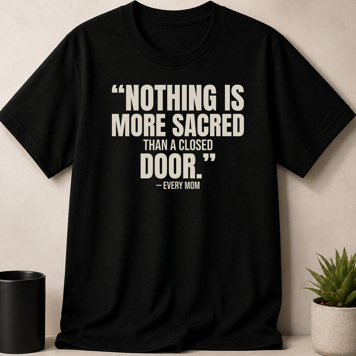 A black crewneck t-shirt featuring the white text "NOTHING IS MORE SACRED THAN A CLOSED DOOR. - EVERY MOM".