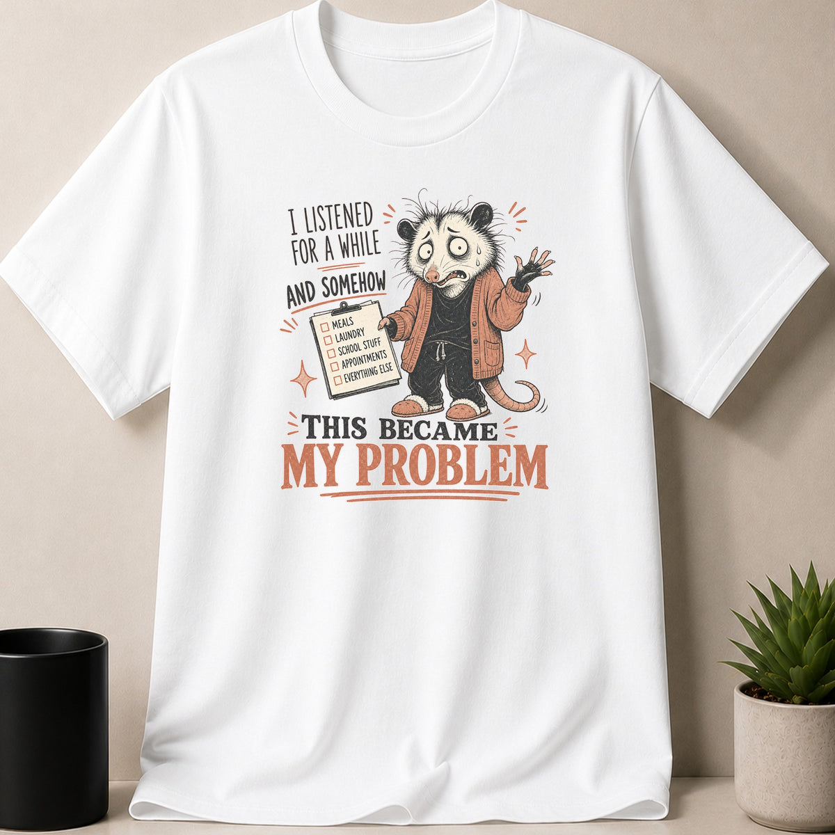 White t-shirt with graphic of stressed possum holding checklist: "THIS BECAME MY PROBLEM".