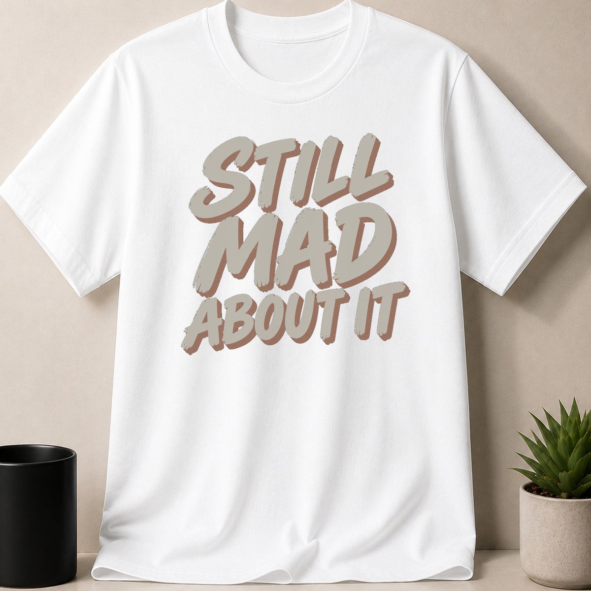White t-shirt with grey text reading "STILL MAD ABOUT IT"