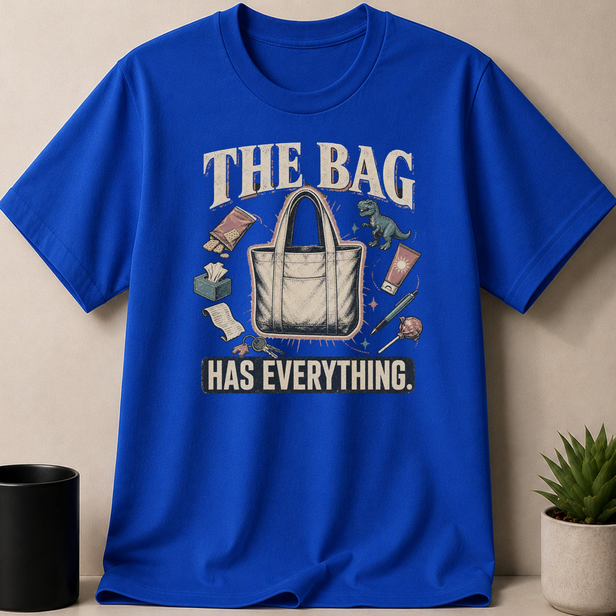 Blue t-shirt with "THE BAG HAS EVERYTHING" text and a tote bag with various items.