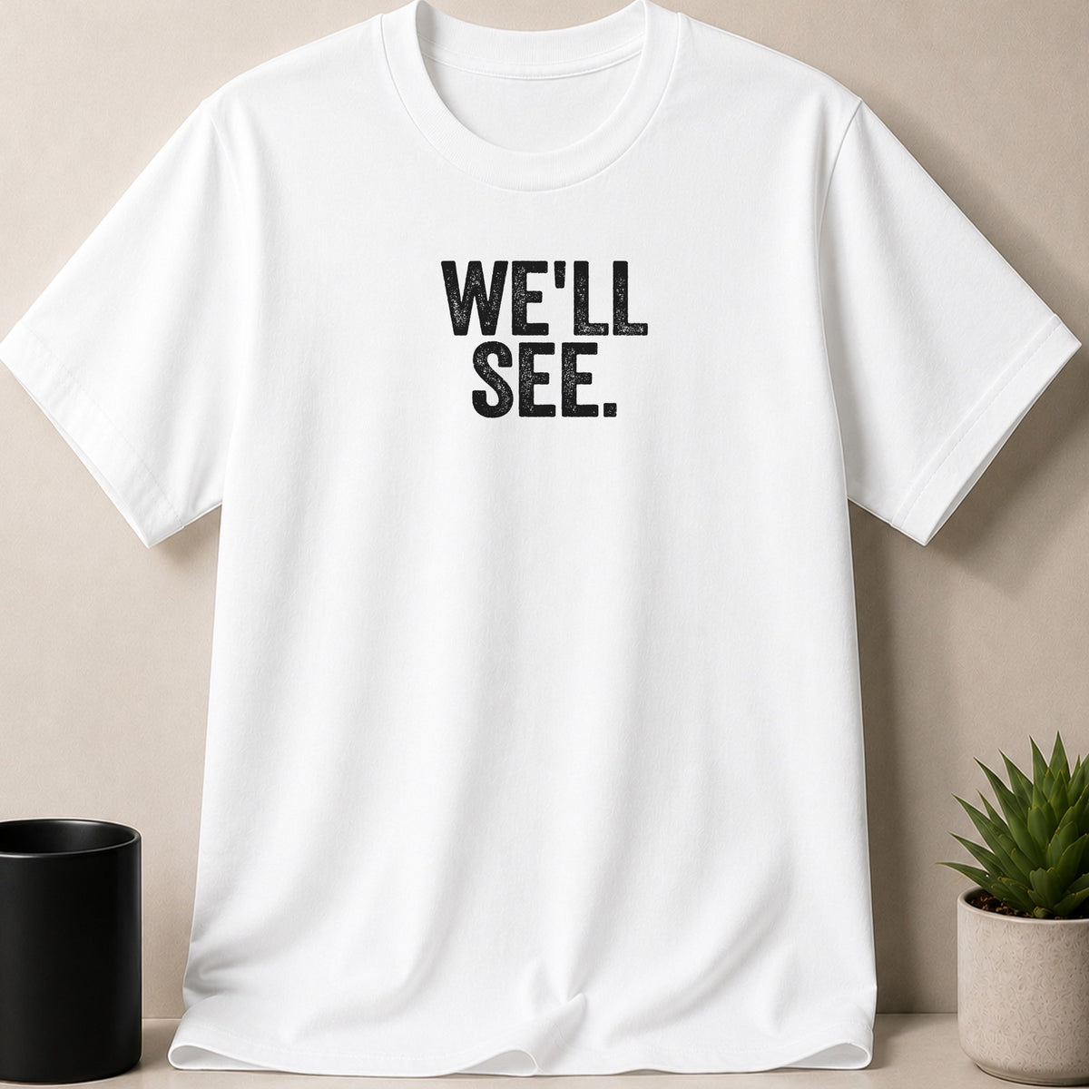 White t-shirt with black text that reads "WE'LL SEE."