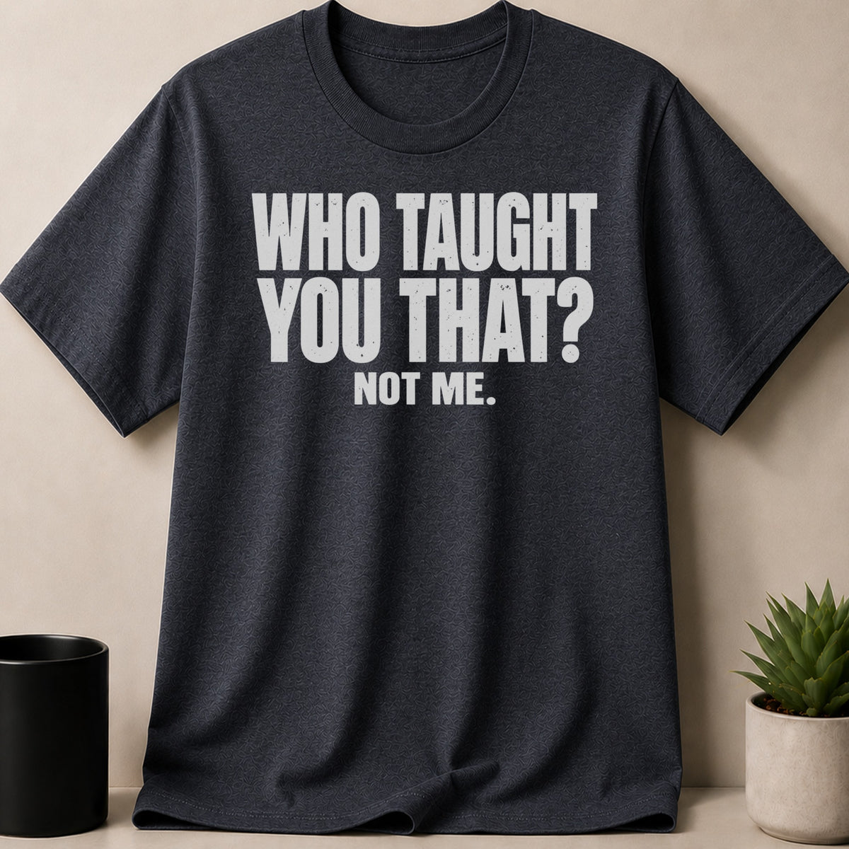 A dark grey t-shirt featuring the white text WHO TAUGHT YOU THAT? NOT ME.