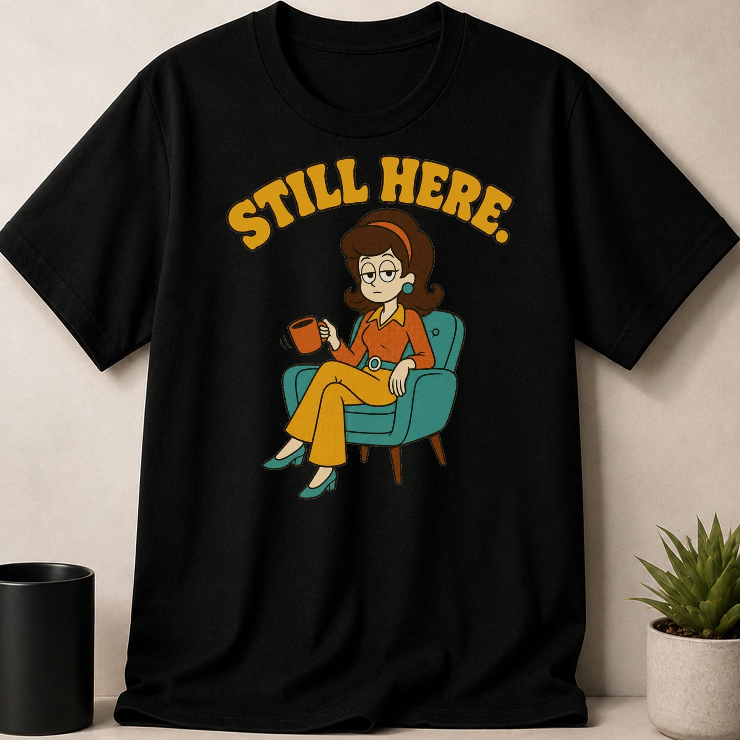 Black t-shirt with yellow text "STILL HERE." and cartoon woman holding coffee.