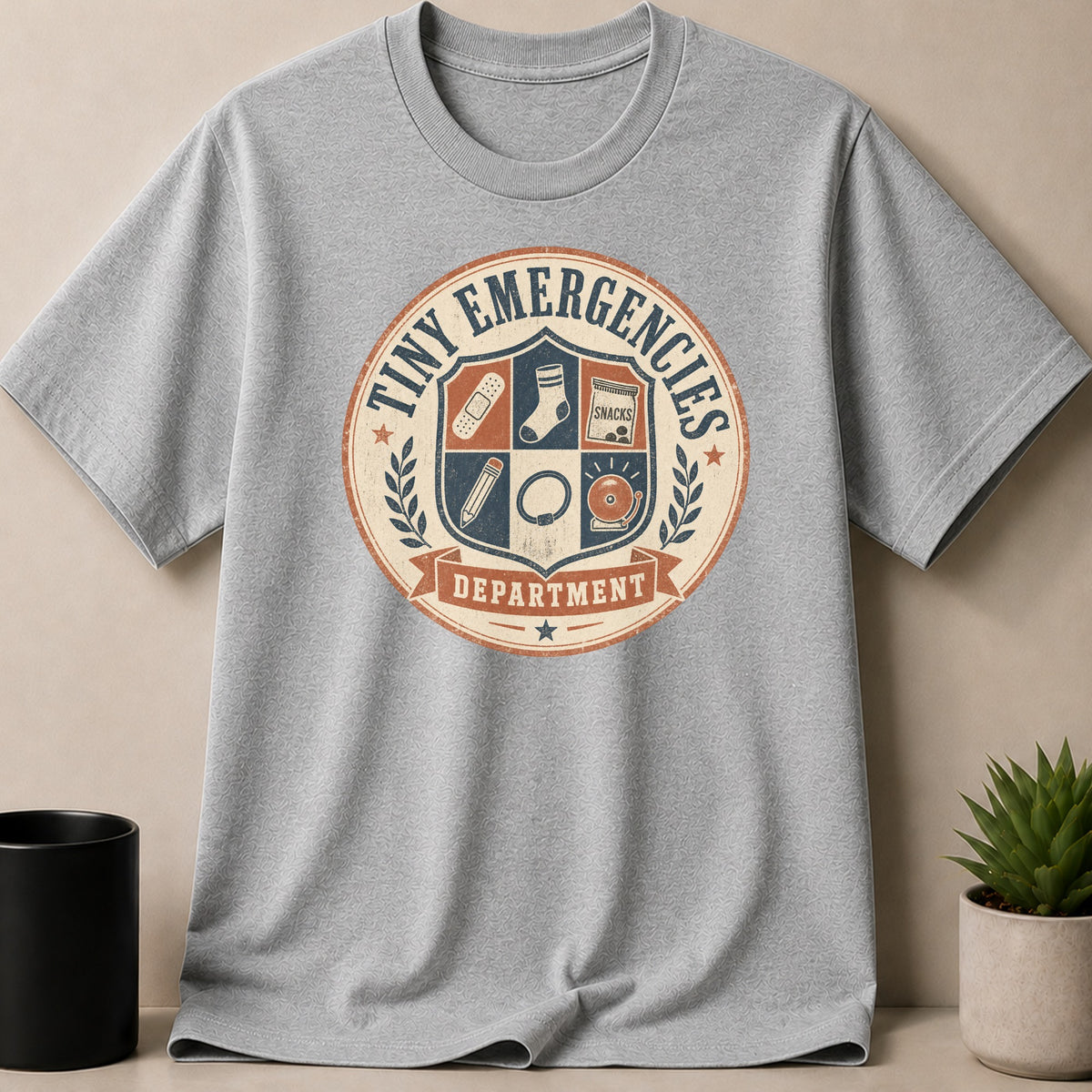 Sport Grey t-shirt — T-shirt with "Tiny Emergencies Department" crest featuring first aid, snacks, pencil, and bell.