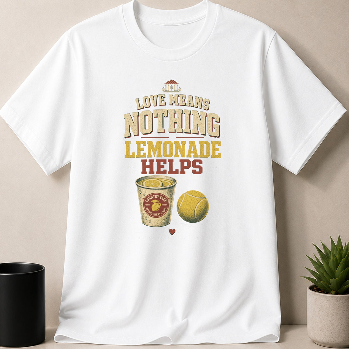 White t-shirt graphic with "Love Means Nothing Lemonade Helps" text, lemonade, and tennis ball.