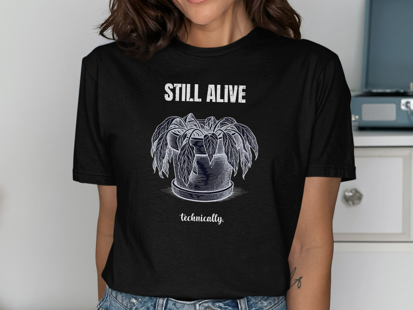 Black t-shirt with white sketch of a wilted plant and text "STILL ALIVE technically".