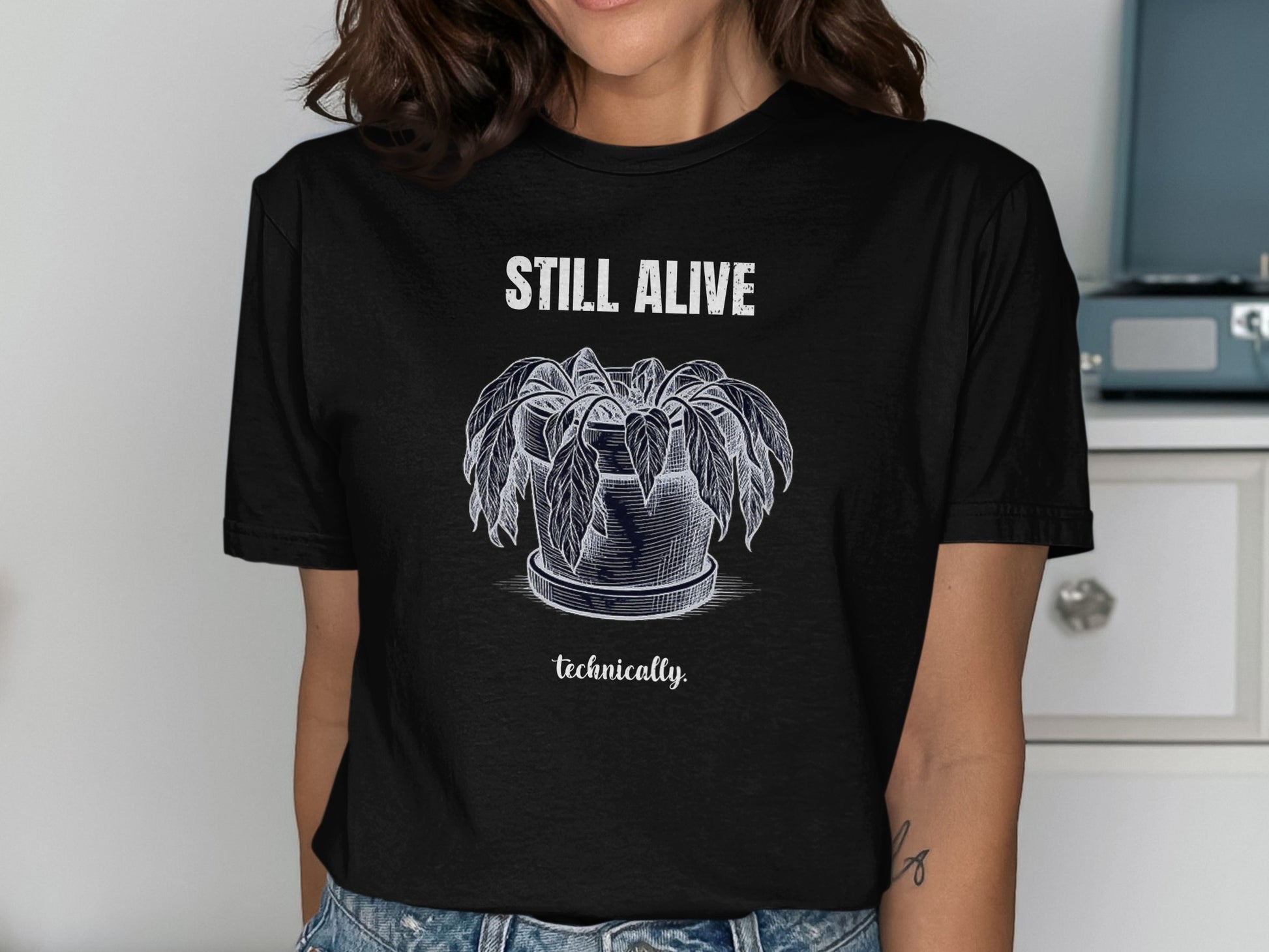 Black t-shirt with white sketch of a wilted plant and text "STILL ALIVE technically".