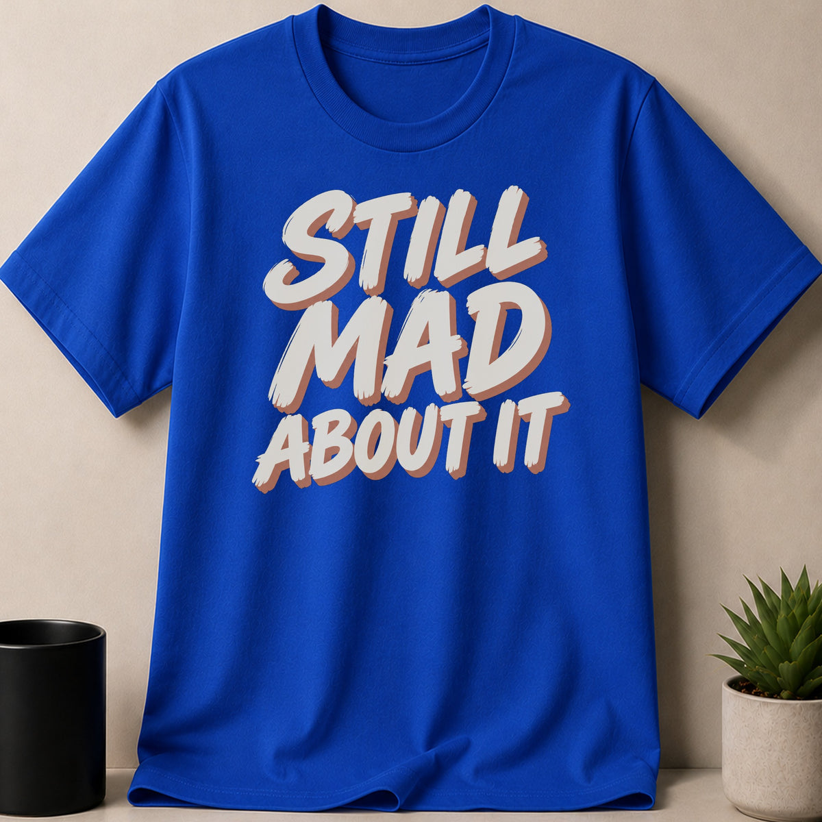 Blue t-shirt with the text "STILL MAD ABOUT IT" in bold, shadow lettering.