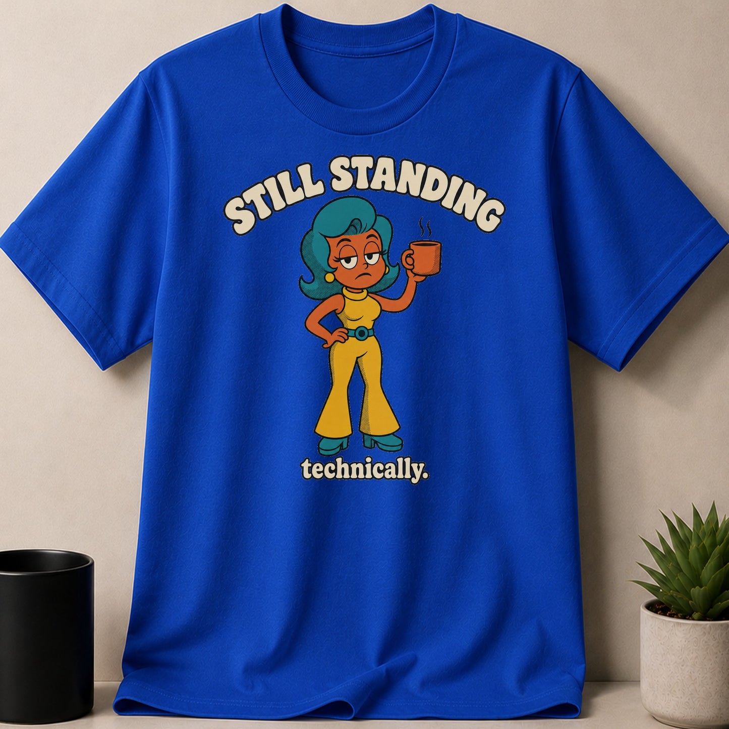Blue t-shirt with cartoon woman holding coffee, text "Still Standing Technically."