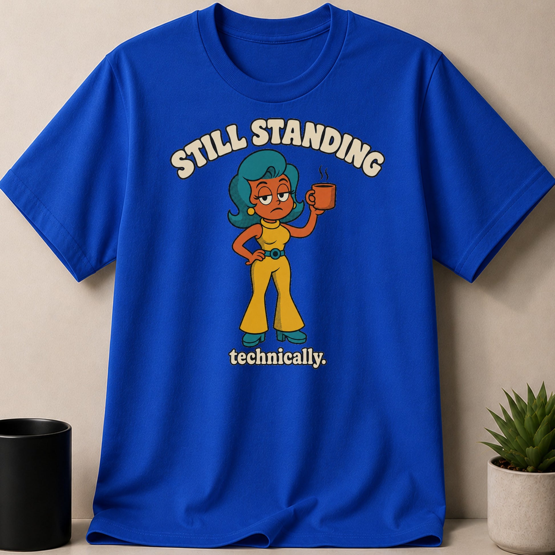 Blue t-shirt with cartoon woman holding coffee, text "Still Standing Technically."