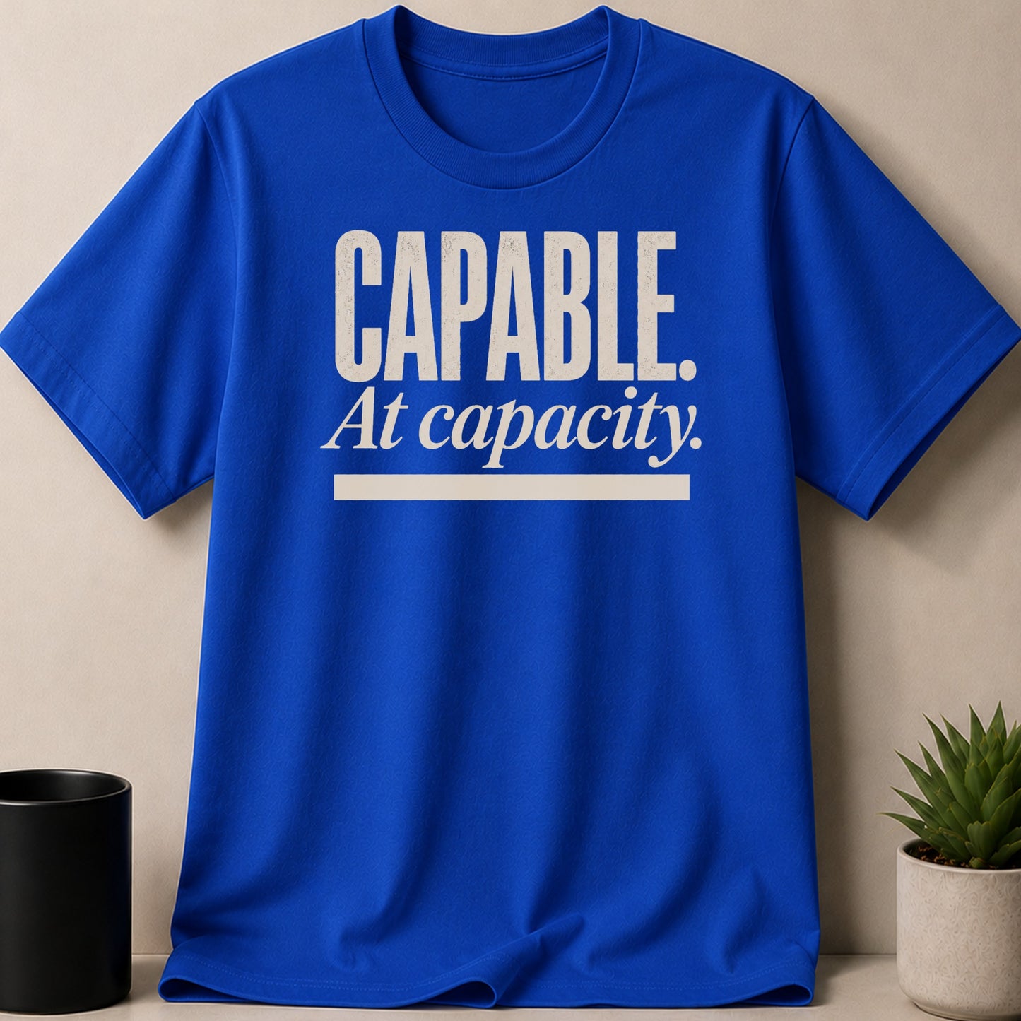 Royal blue t-shirt with white text reading "CAPABLE. At capacity."