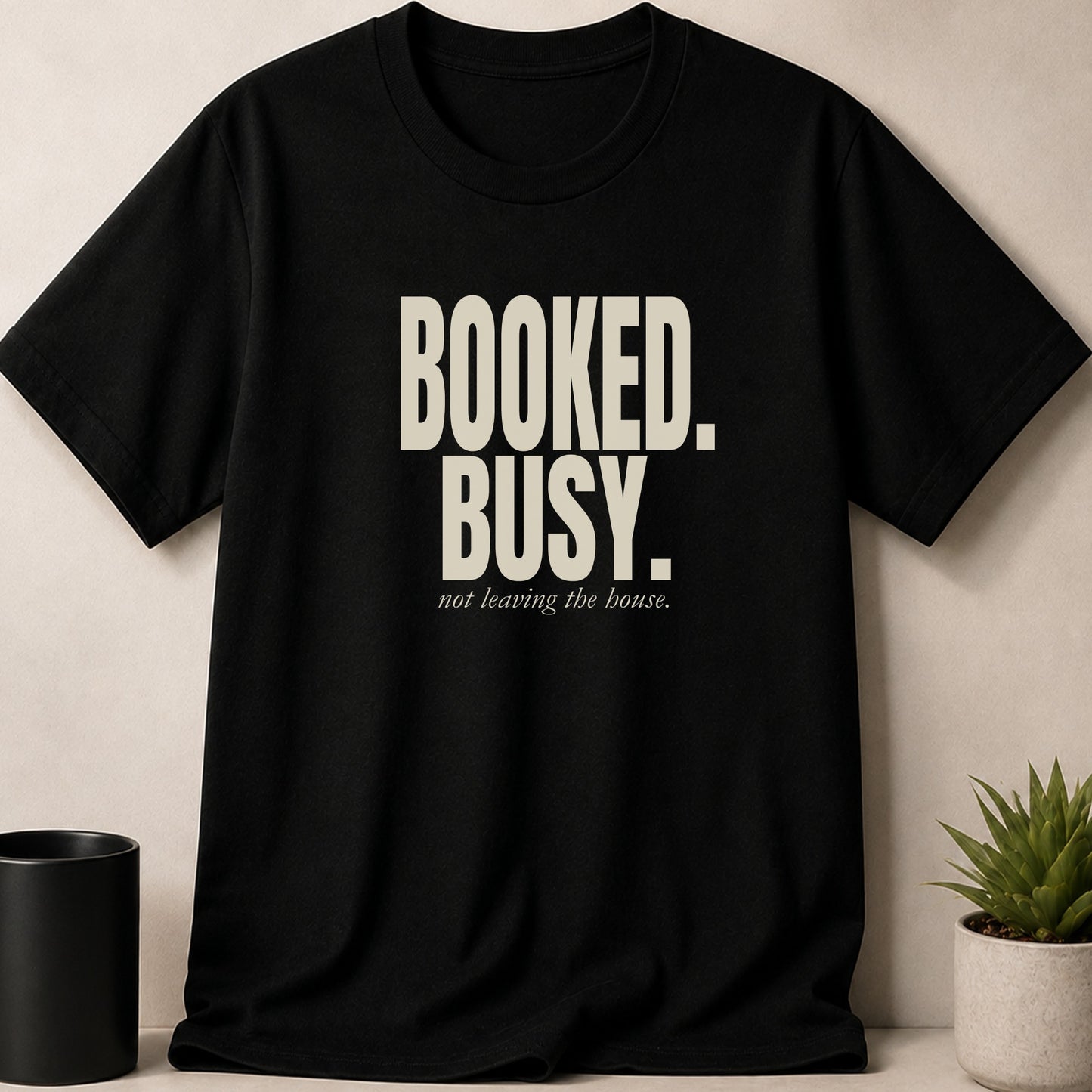 Black t-shirt with text "BOOKED. BUSY. not leaving the house."