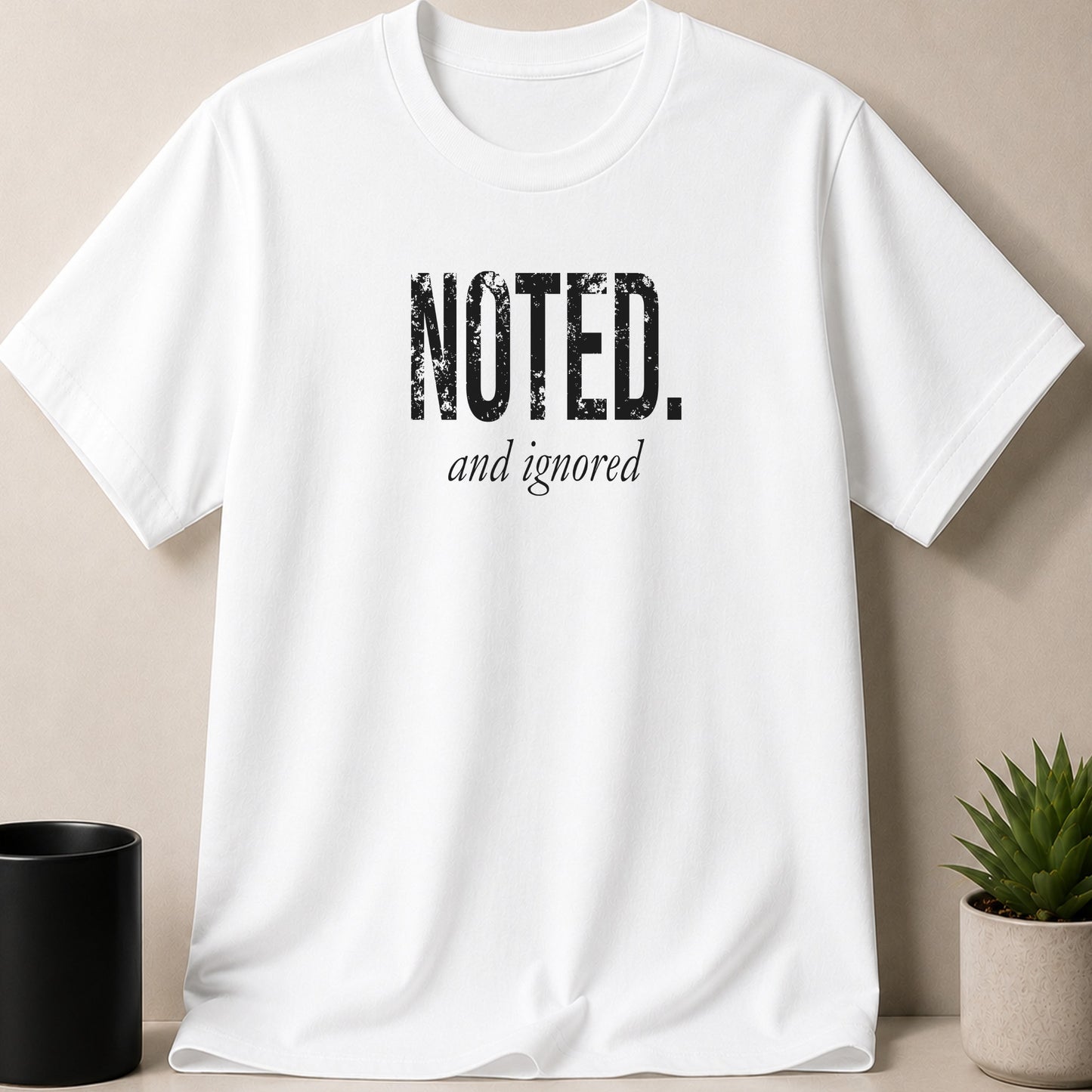 White t-shirt with "NOTED. and ignored" text in black distressed font.
