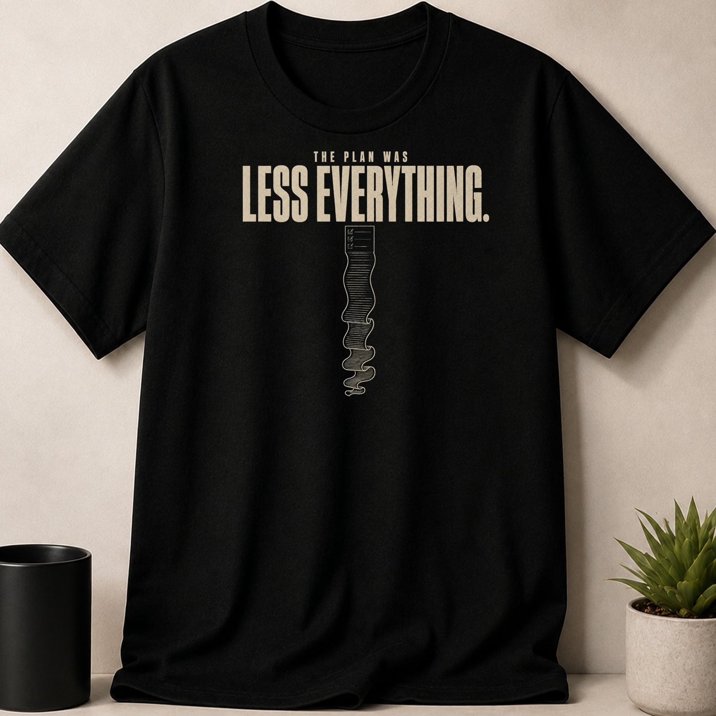 Black t-shirt with text "THE PLAN WAS LESS EVERYTHING." and a scroll graphic.