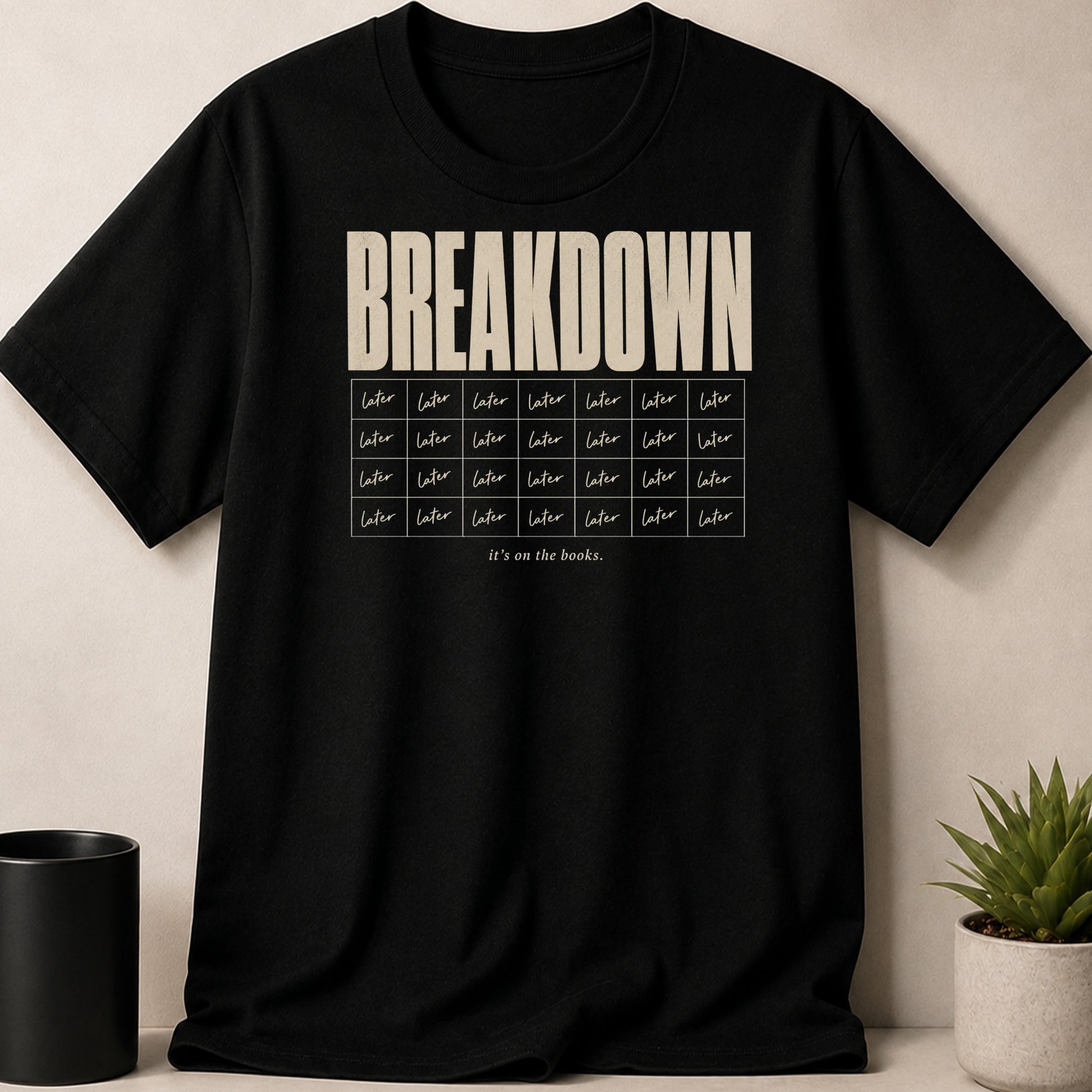 Black t-shirt with "BREAKDOWN" text above rows of "later" and "it's on the books."