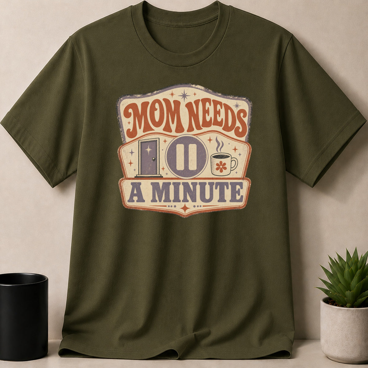 Green t-shirt with "Mom Needs A Minute" graphic featuring a door, pause icon, and coffee cup.