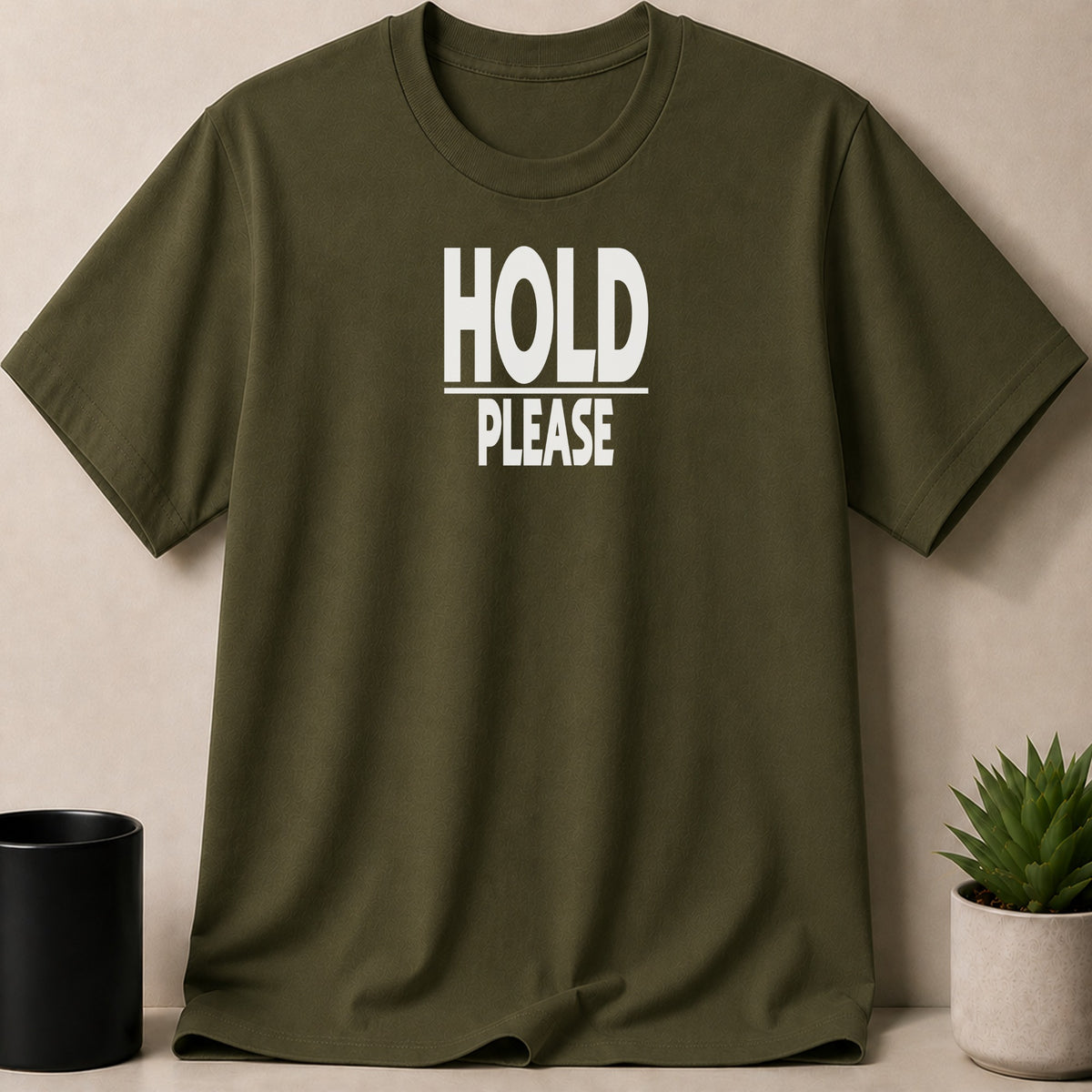 Olive green t-shirt with white text "HOLD PLEASE" on the front.