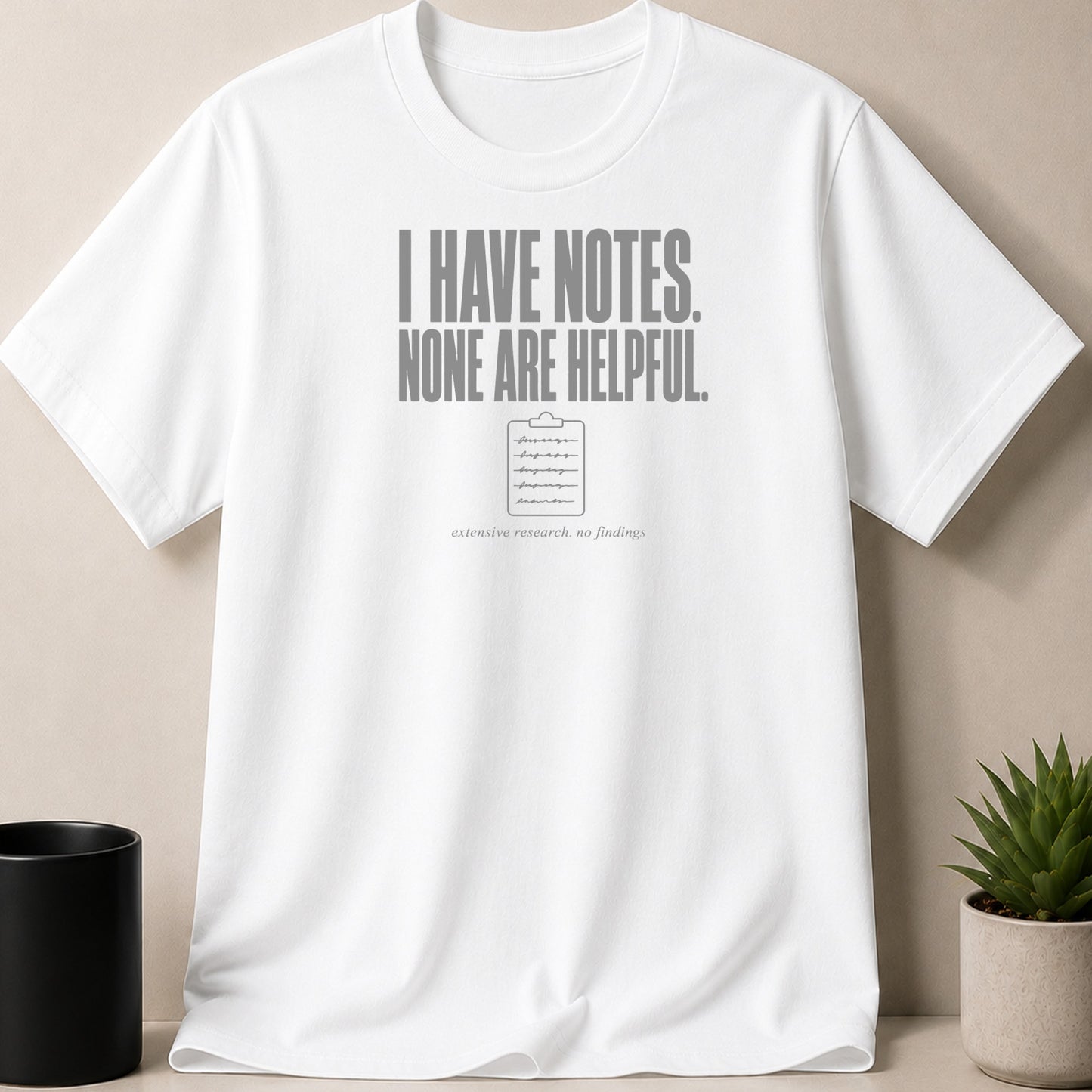 White t-shirt with text "I HAVE NOTES. NONE ARE HELPFUL." and a clipboard graphic.