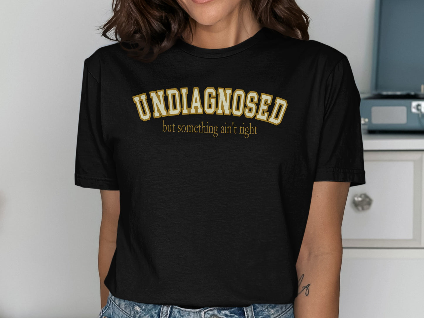 Black t-shirt with "UNDIAGNOSED but something ain't right" in gold lettering.