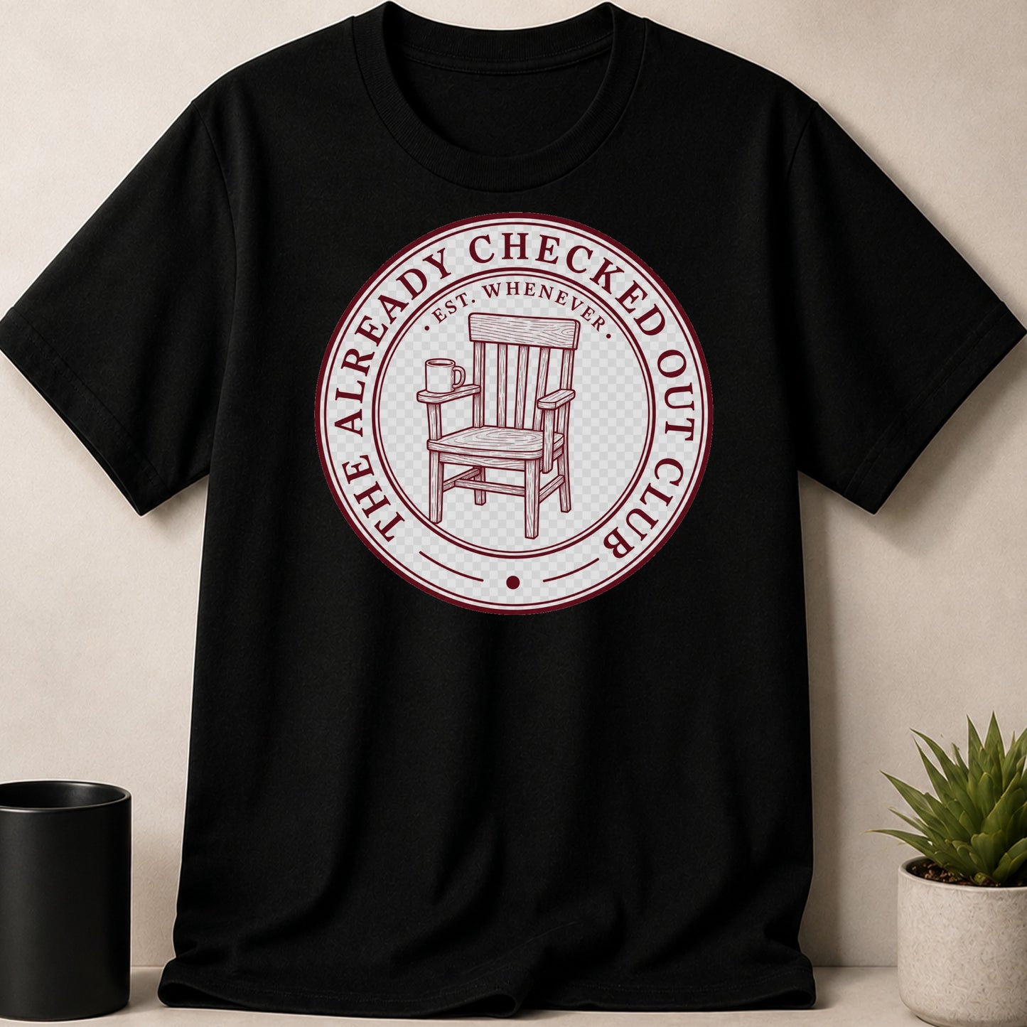 Black t-shirt with a circular graphic of an armchair and mug, text "The Already Checked Out Club".