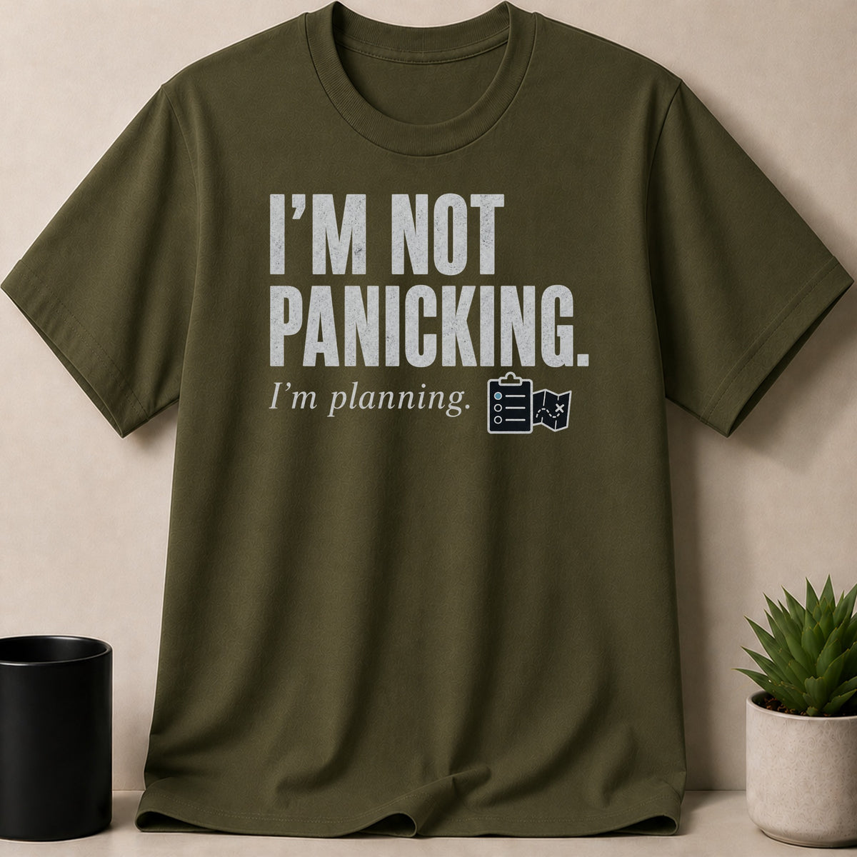 Olive green t-shirt with white text "I'M NOT PANICKING. I'm planning." and icons.