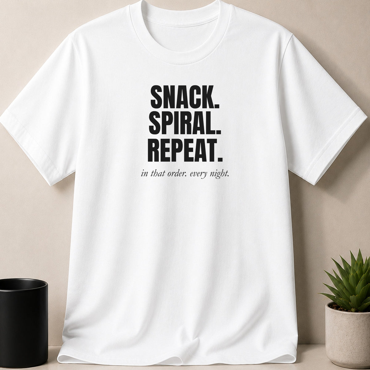 White t-shirt with black text "SNACK. SPIRAL. REPEAT. in that order. every night."