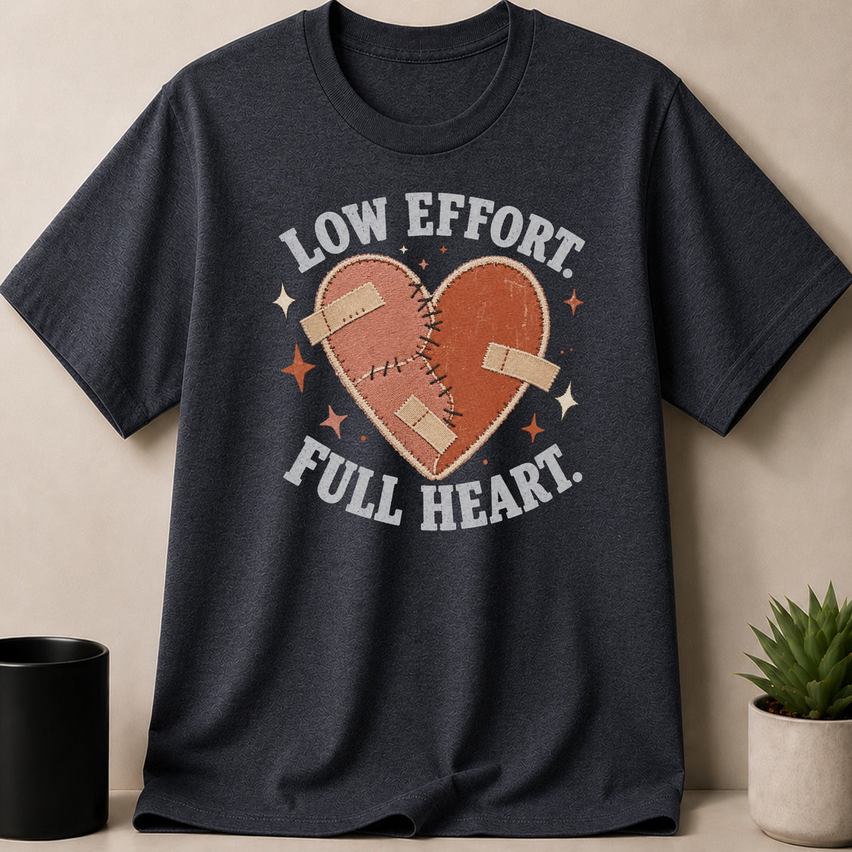 Dark grey t-shirt with a patched heart graphic and text "LOW EFFORT. FULL HEART."