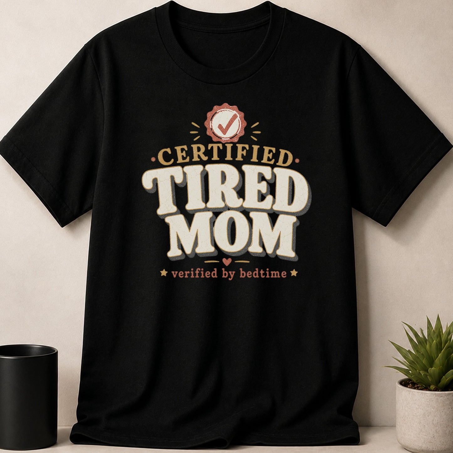 Black t-shirt with "CERTIFIED TIRED MOM verified by bedtime" text and checkmark badge.