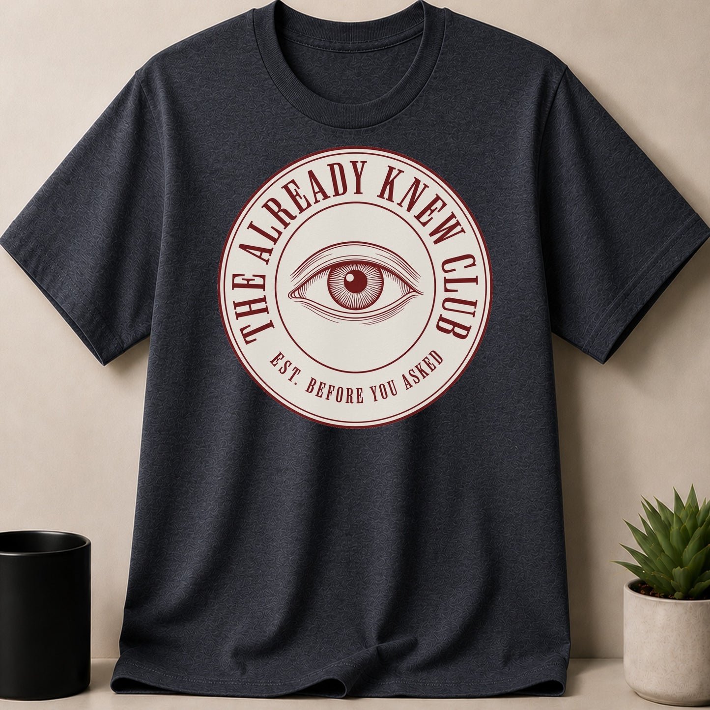 Dark t-shirt with iconic eye design and text "The Already Knew Club."