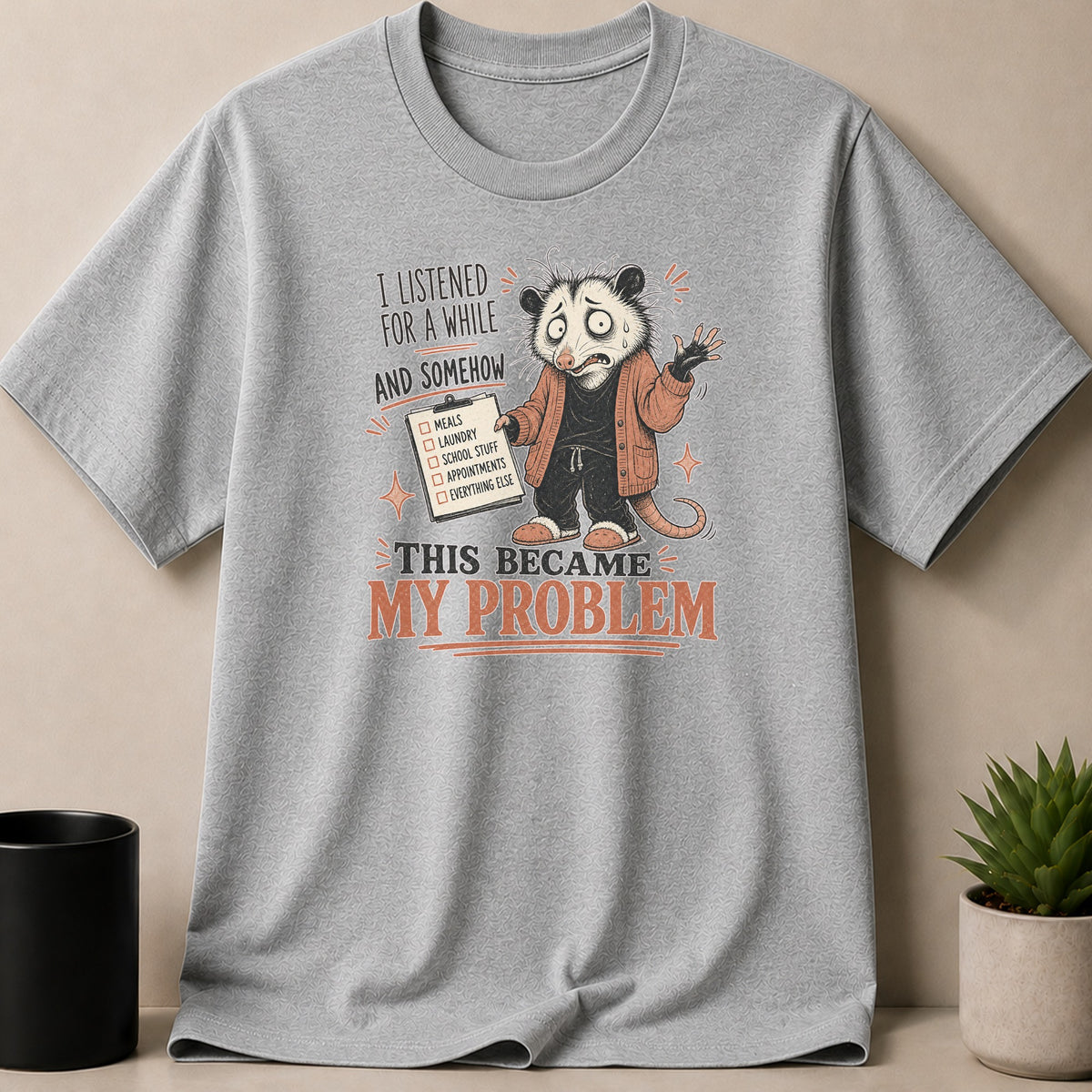 Gray t-shirt with illustration of a stressed possum holding a list titled "This Became My Problem".