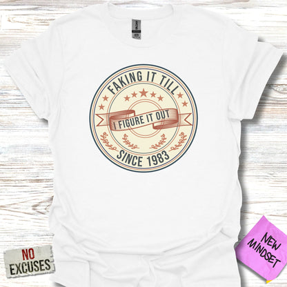 White t-shirt with "Faking It Till I Figure It Out Since 1983" graphic.